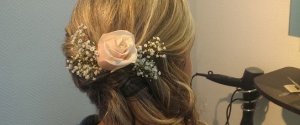 Eine Frau mit langen blonen Haaren hat eine neue Frisur für die Hochzeit bekommen, mit Rosengesteck